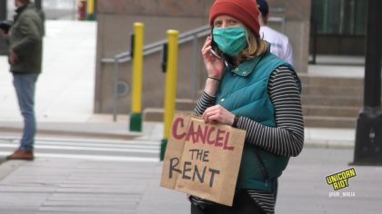 Masked person on the phone holds "cancel the rent" sign