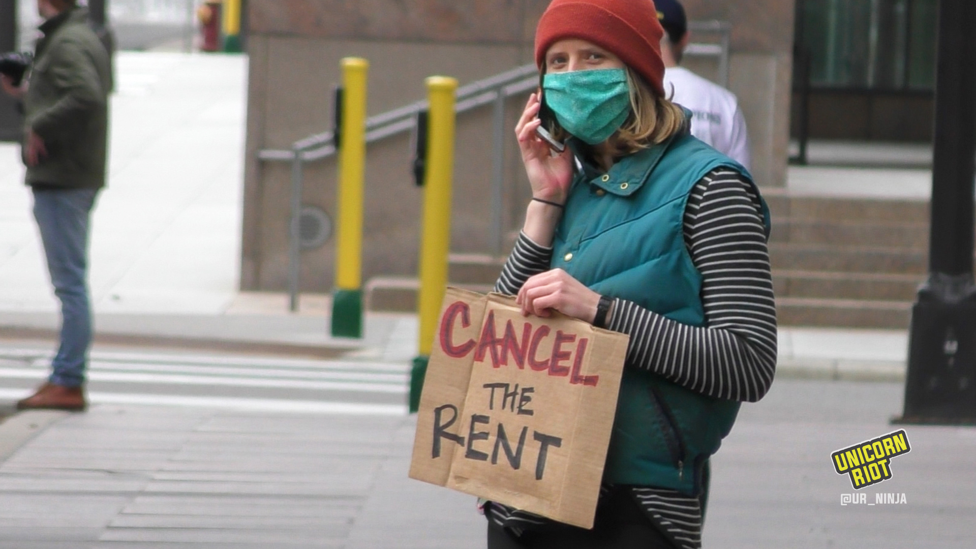 Masked person on the phone holds "cancel the rent" sign