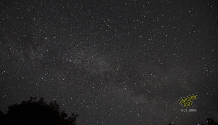 image: ten-second long exposure shot of the night sky facing East, in the northern hemisphere at midsummer. The nebulous arm of our spiral galaxy The Milky Way is visible stretching across the night sky from right to left in the image.