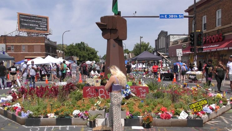 A large circular garden with a fist and a red black and green flag on top sit in the middle of the intersection of 38th and Chicago