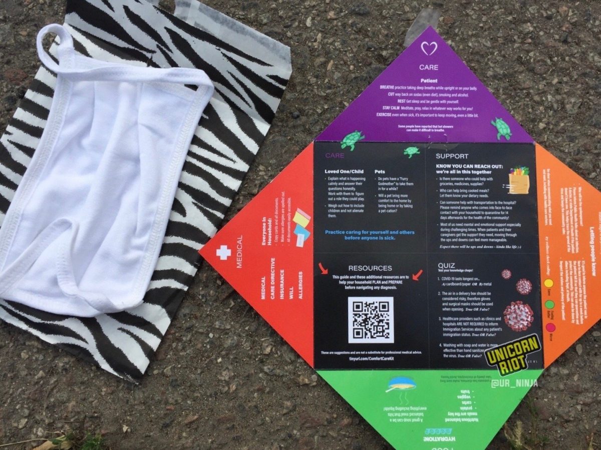 image: a white cloth mask rests atop a white paper envelope printed with black zebra print stripes. Beside this is a handout with information about preventing coronavirus infection, and what to do if/when one has contracted the virus. 