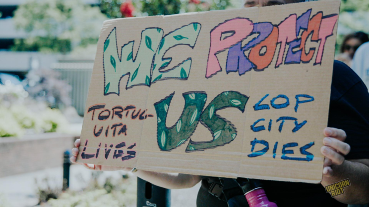 A cardboard protest sign reads "We Protect Us - Tortuguita Lives - Cop City Dies"
