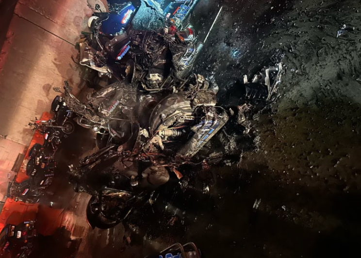 Crime scene photo showing burnt-out Atlanta Police motorcycles in a parking lot at the Atlanta Police Training Academy. The image is washed in a red and blue light presumably from a police or fire department vehicle from out-of-frame.