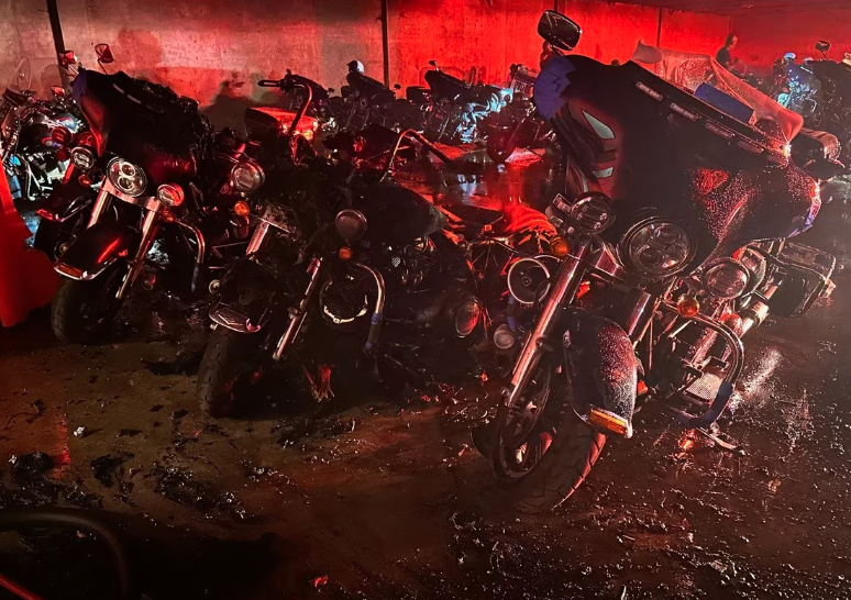 Crime scene photo showing burnt-out Atlanta Police motorcycles in a parking lot at the Atlanta Police Training Academy. The image is washed in a red light presumably from a police or fire department vehicle from out-of-frame.