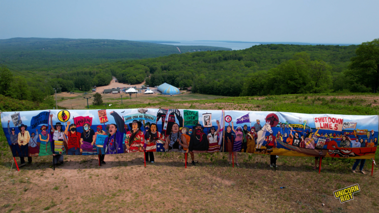 Water protectors gathered on a hill near Ashland, Wisconsin with a 48 foot by 6 foot banner that depicts activists from the Line 3, NoDAPL, and Line 5 movements