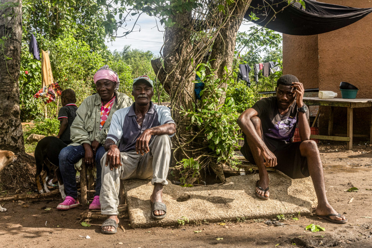 A middle-aged sugar cane cutter, his wife, and their son pose for a seated family photo in front of a tree.