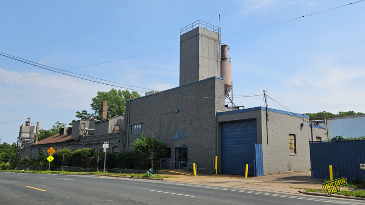 Blue Sky with scattered clouds, Smith Foundry Asphalt factory building towering in the middle of the frame with a street and street signs on the side