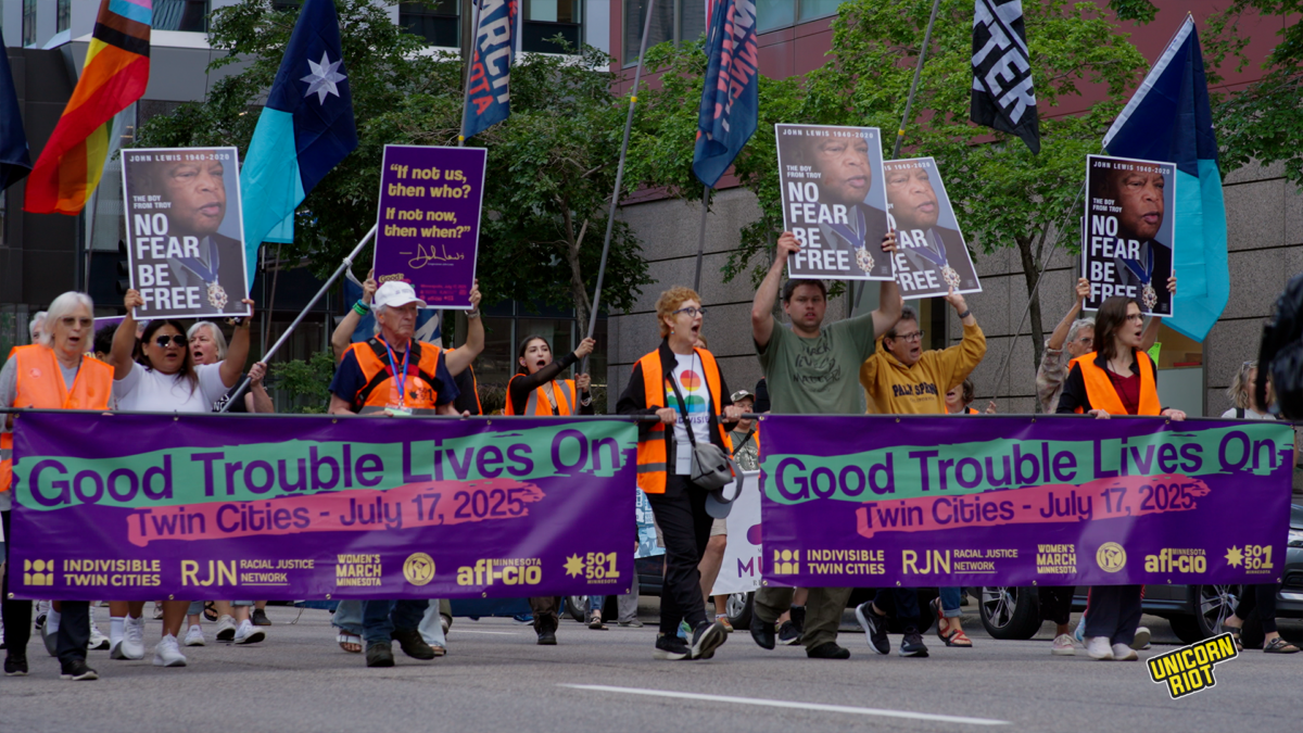 marshals with orange vests holding banners with good trouble lives on twin cities - july 17, 2025 sponsored by Indivisible Twin Cities Racial Justice Network Womens March Minnesota, AFLCLO 50501 Minnesota